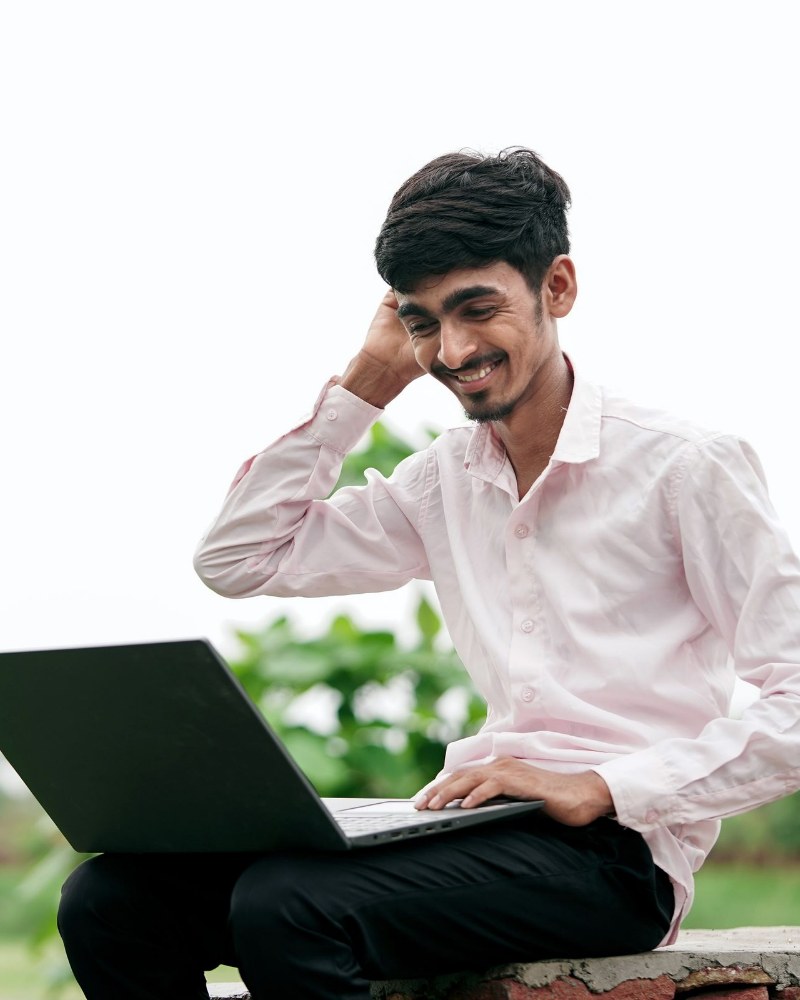Ishaan Kapoor smiling at his laptop, outdoors
