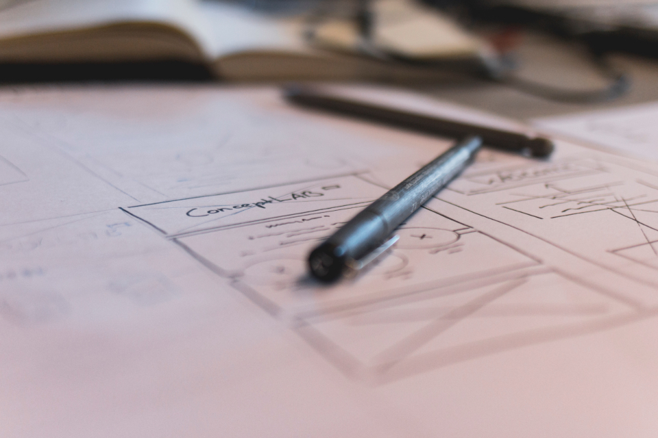 A paper wireframe of a phone screen with a pen